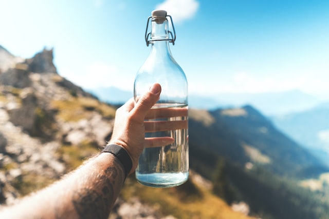 man holding water bottle outside with mountains in background